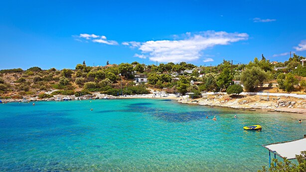 A coastal area with clear turquoise waters, a rocky shoreline, and buildings on a hillside. - Iliaktis Xenios Zeus  (Νήσοι)