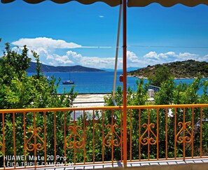 Ein Balkon mit Blick auf eine Küstenlandschaft, darunter ein Boot auf dem Wasser und ferne Hügel.