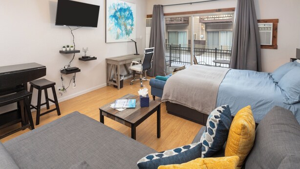 Een moderne hotelkamer met een flatscreen-tv, een bureau met stoel, een bank en een balkon met uitzicht.
