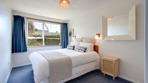 Une chambre avec un grand lit, une fenêtre avec des rideaux, une table de chevet, un miroir fixé au mur et une petite armoire en bois.