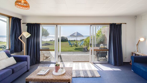 Un salon moderne avec un canapé, une table basse et une vue sur l’océan et une montagne, grâce à de grandes portes vitrées.
