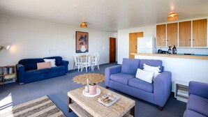 Un salon moderne avec un canapé bleu, un canapé violet, une table basse et un coin repas avec des chaises blanches.