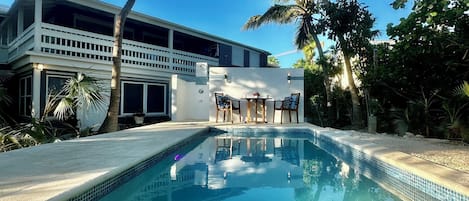 A swimming pool with a tiled edge, surrounded by palm trees and a building with a balcony.