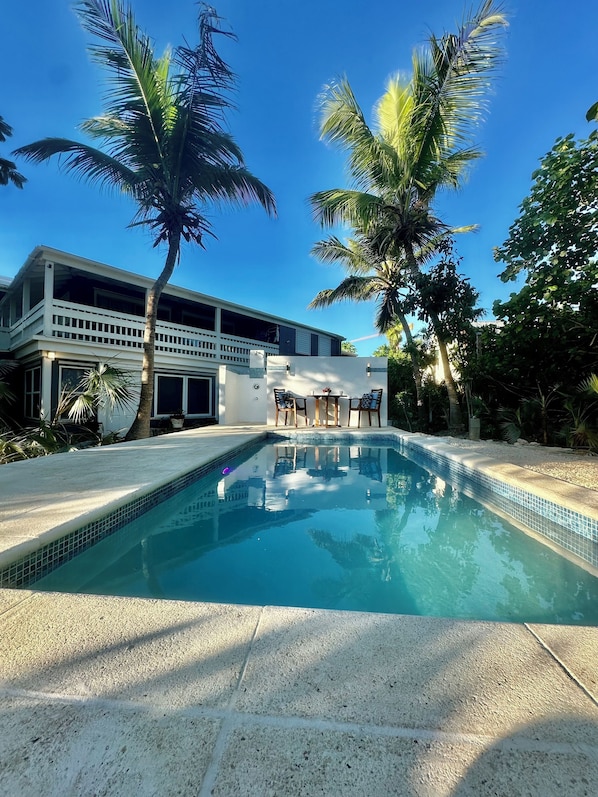 A swimming pool with a tiled edge, surrounded by palm trees and a building with a balcony.