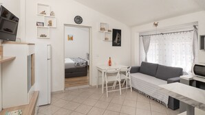 Ett kompakt bostadsutrymme med ett litet kök, en matplats, en soffa och en TV.