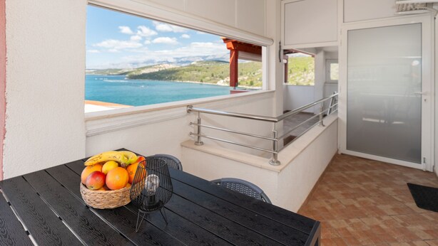 En balkong med utsikt över havet, ett bord med frukt och ett modernt kök.