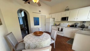 Une cuisine avec des meubles blancs, un four à micro-ondes, un four traditionnel et un coin repas comprenant une table et des chaises.