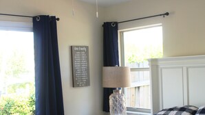 Une chambre à coucher comprenant un lit, une table de chevet, une lampe, un ventilateur de plafond et une fenêtre avec des rideaux.