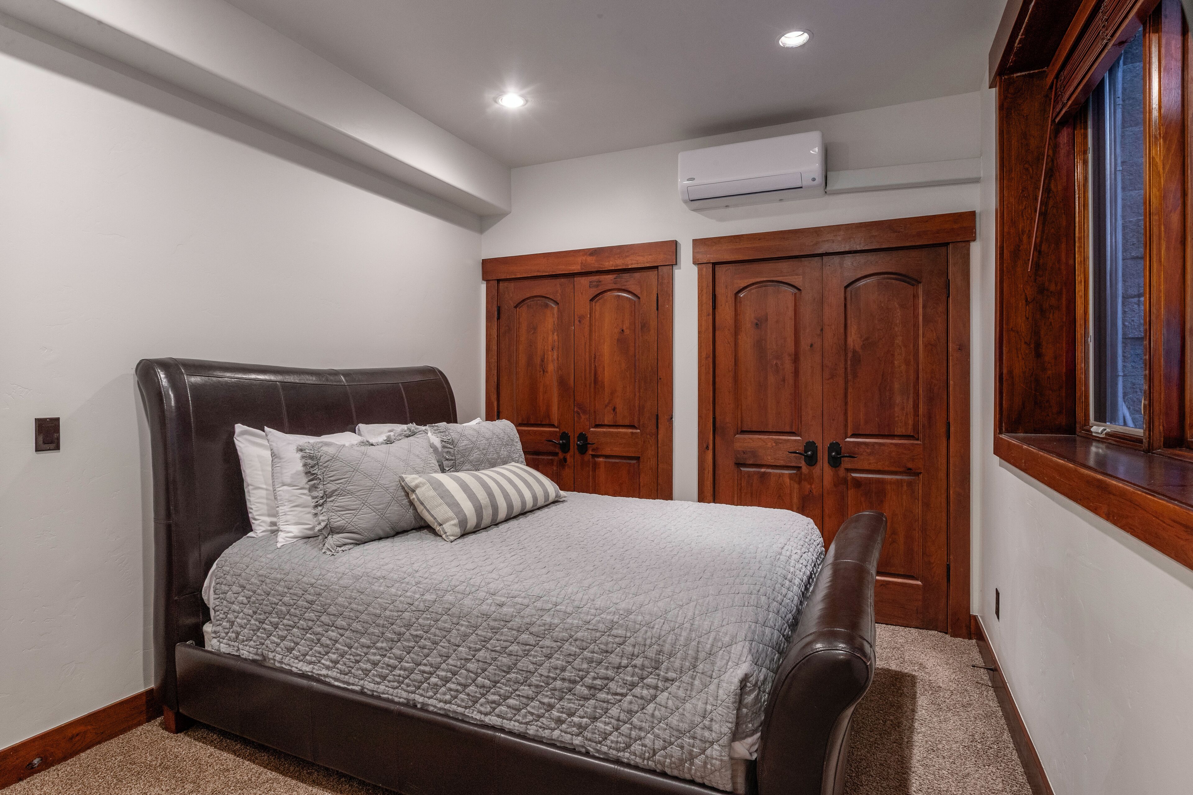 A bedroom with a dark brown bed, a gray quilted bedspread, and two wooden doors.