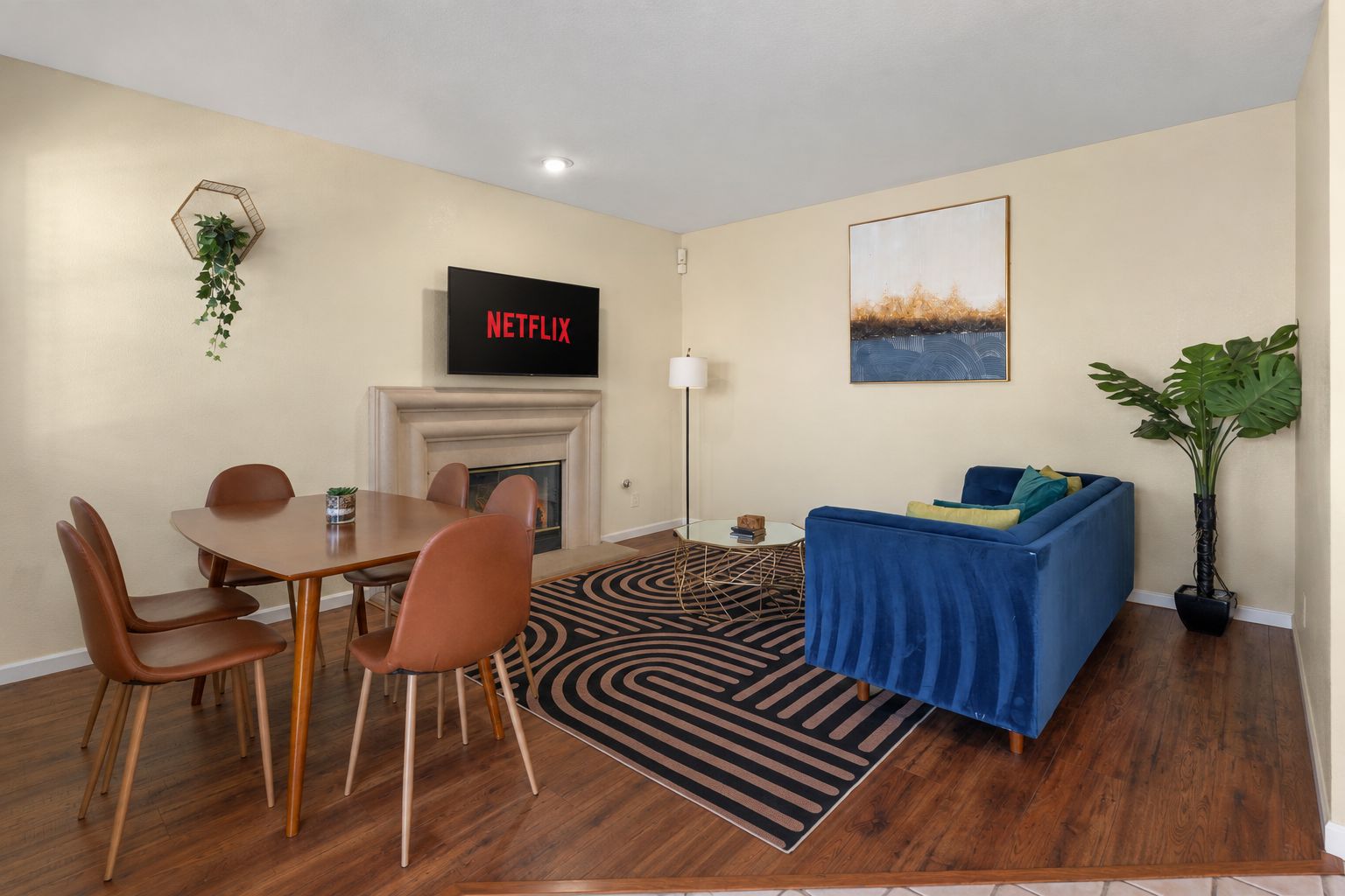Ein Wohnzimmer mit Kamin, einem blauen Sofa, einem Esstisch mit Stühlen und einem Flachbildfernseher, der 'NETFLIX' zeigt.
