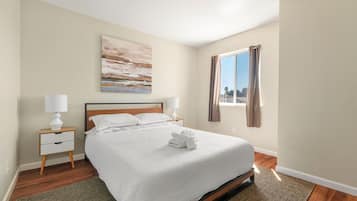 A neatly arranged bedroom with a bed, two bedside tables, a window with curtains, and a painting on the wall.