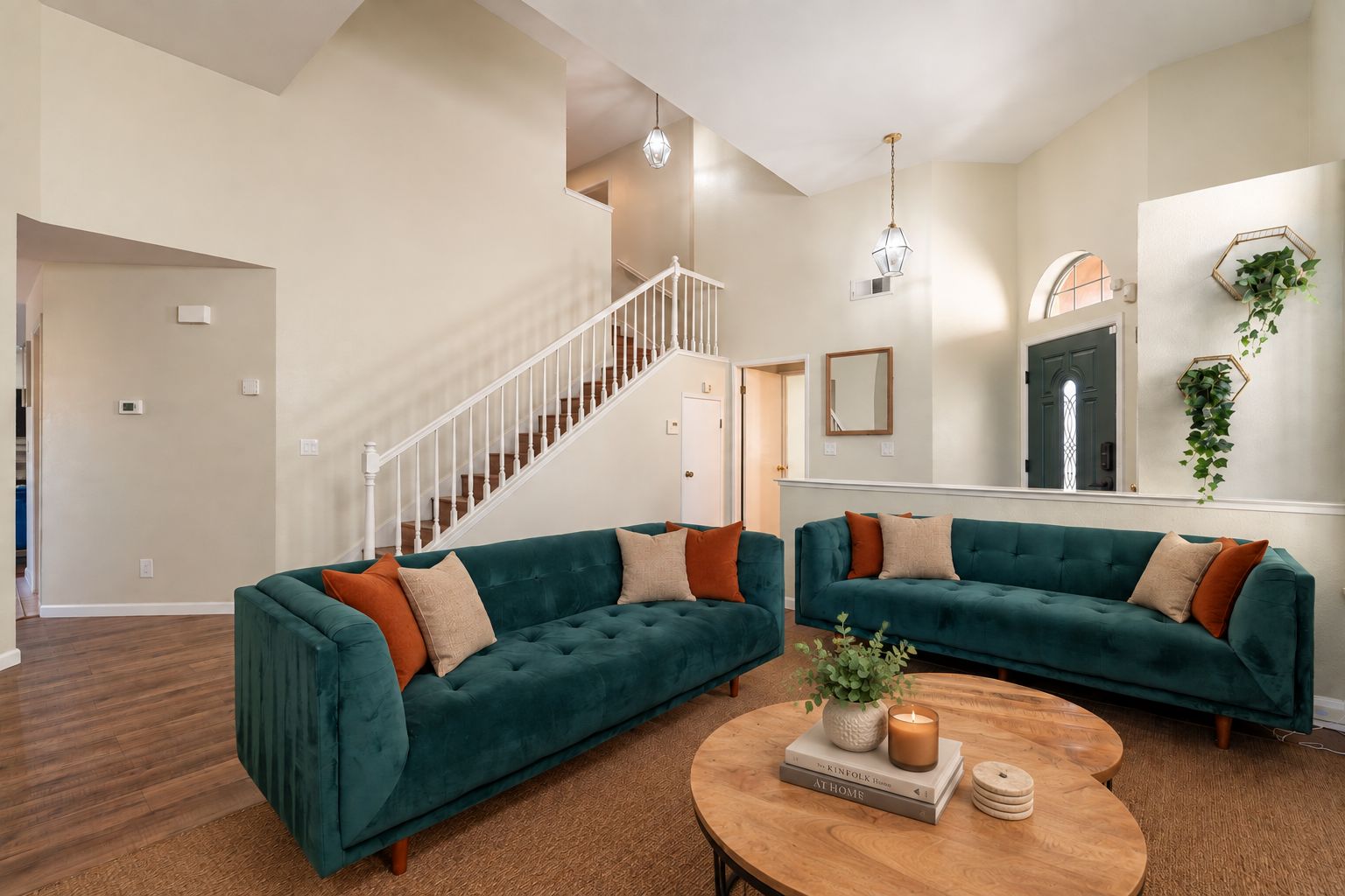 A spacious living room with two teal sofas, a wooden coffee table, and a staircase leading to another level.