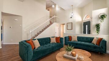 A spacious living room with two teal sofas, a wooden coffee table, and a staircase leading to another level.