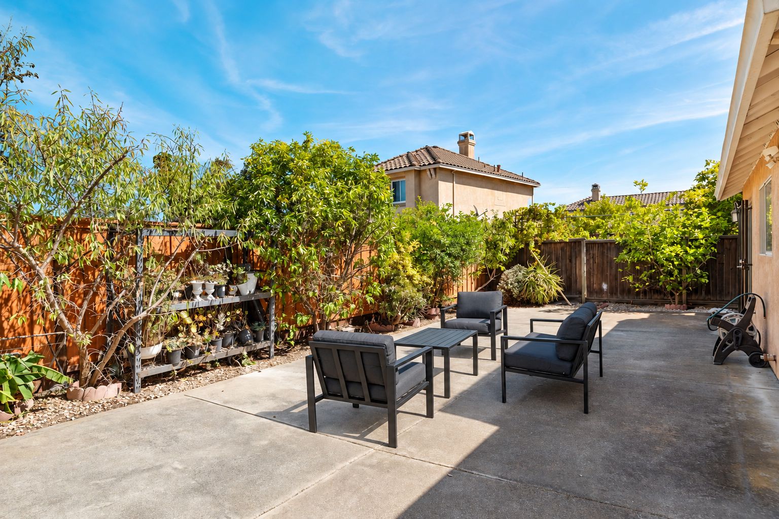 A patio with outdoor furniture, a wooden fence, and various potted plants.