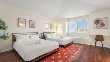 A hotel room with two beds, a red patterned rug, a desk with a chair, and artwork on the walls.
