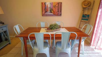 A dining area with a wooden table, four light blue chairs, a potted plant, and a painting of a street scene on the wall.