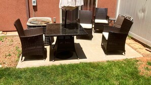 An outdoor patio with a glass table and wicker chairs, a white umbrella, and a small air conditioning unit.