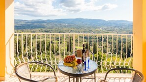 A balcony with a table set for two, featuring a bottle and glasses, and a plate of fruit.