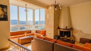 A spacious living room with a stone fireplace, large windows offering a mountain view, and a cozy seating area.