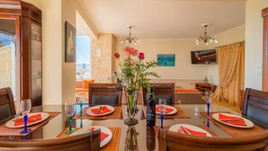 A dining area with a round table set for four, featuring clear glassware, red napkins, and a bottle of wine.