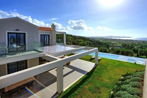 Une maison moderne dotée d’un balcon en verre donnant sur un paysage verdoyant et luxuriant, ainsi que sur une piscine.