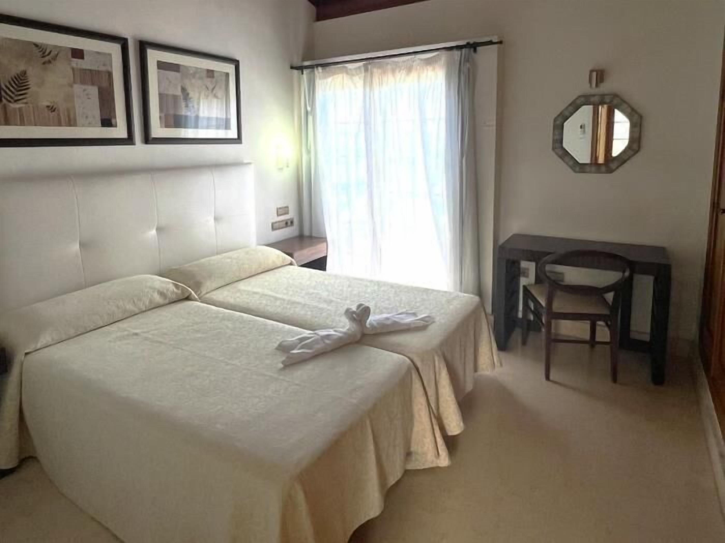 Una cama doble con cabecera, un escritorio con silla y un espejo en la pared.