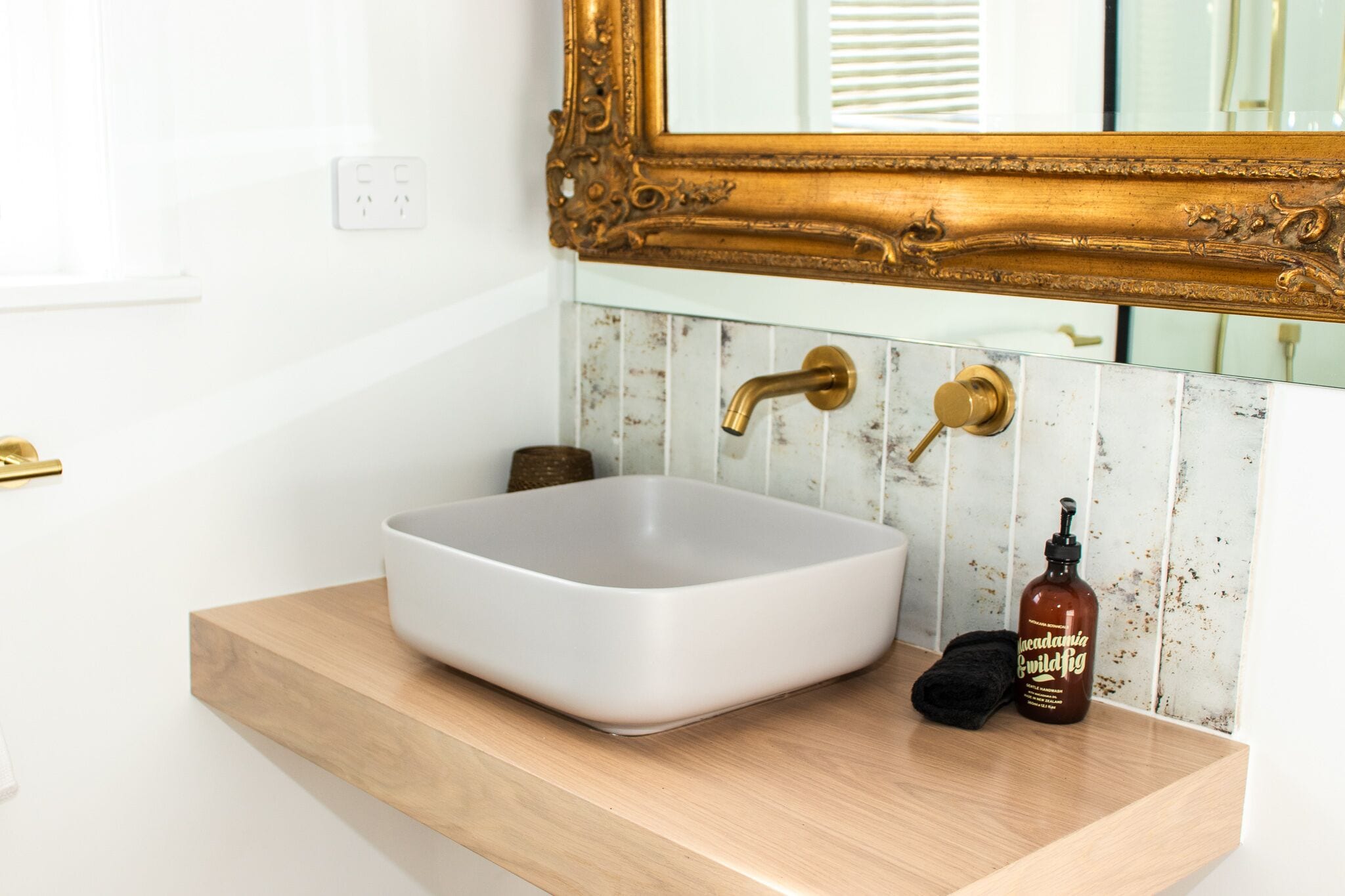A bathroom with a white sink, gold faucets, and a mirror with an ornate gold frame.