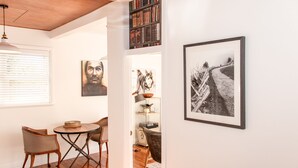 Una habitación acogedora con techo de madera, una mesa redonda con sillas, una estantería y una fotografía en blanco y negro enmarcada en la pared.
