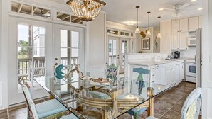 A spacious kitchen with white cabinets, a glass dining table, and a chandelier.