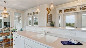 A modern kitchen with white cabinetry, a large island with a sink, pendant lighting, and large windows.