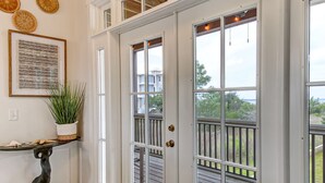 A foyer with a wooden floor, a potted plant, a framed artwork, and a door leading to a deck.