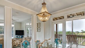 A spacious living room with a glass dining table, wicker chairs, and a chandelier.