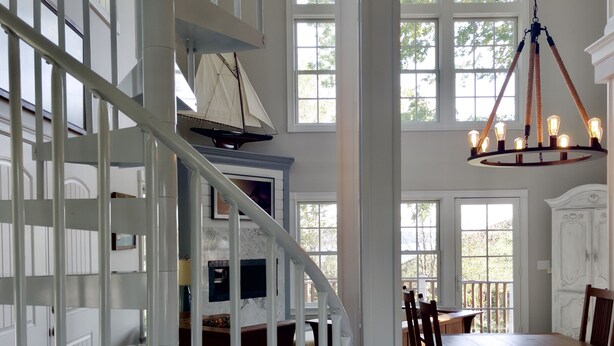 A spacious interior with a white spiral staircase, a dining area with wooden furniture, and large windows allowing natural light. - Beautiful Modern Cottage with Private Lake Access (Skaneateles)