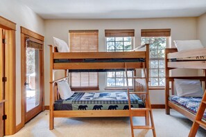 A bunk bed room with a ladder, a window with blinds, and a door with a view of the outside.