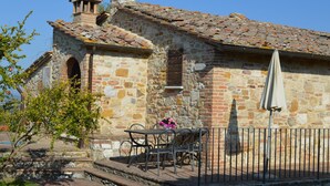 A stone building with a tiled roof, a chimney, and a small table with chairs.