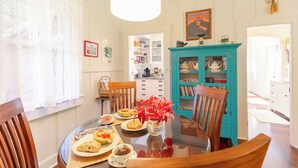 A dining area with a round table, chairs, a vase with flowers, and a teal cabinet. - Historic Turn-of-the-Century Bungalow in the heart of Volcano Village. (Volcano)