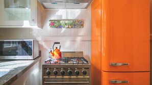 A kitchen with a gas stove, a microwave, and an orange refrigerator. - Historic Turn-of-the-Century Bungalow in the heart of Volcano Village. (Volcano)