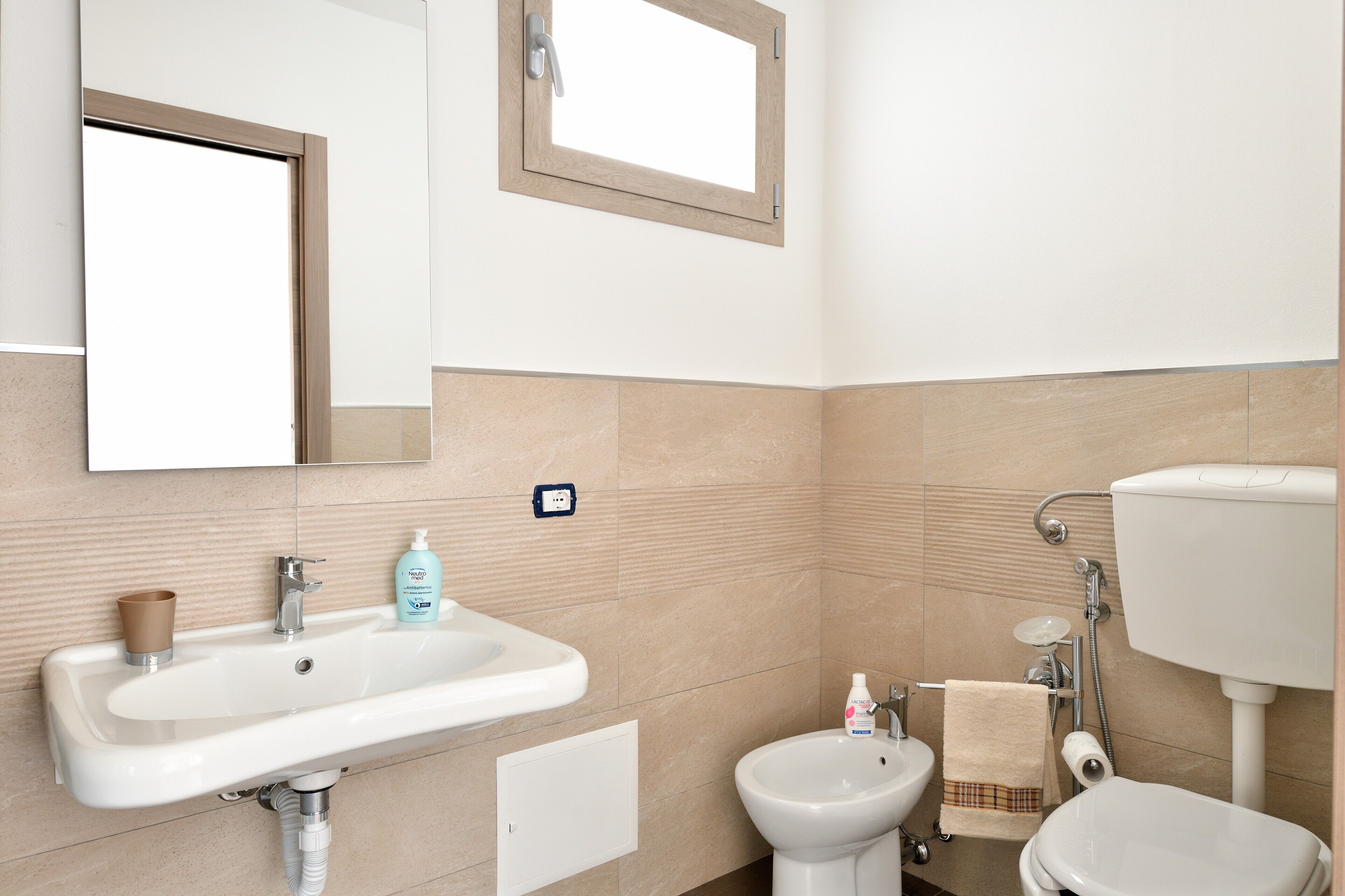 A bathroom with a sink, bidet, toilet, mirror, and window.