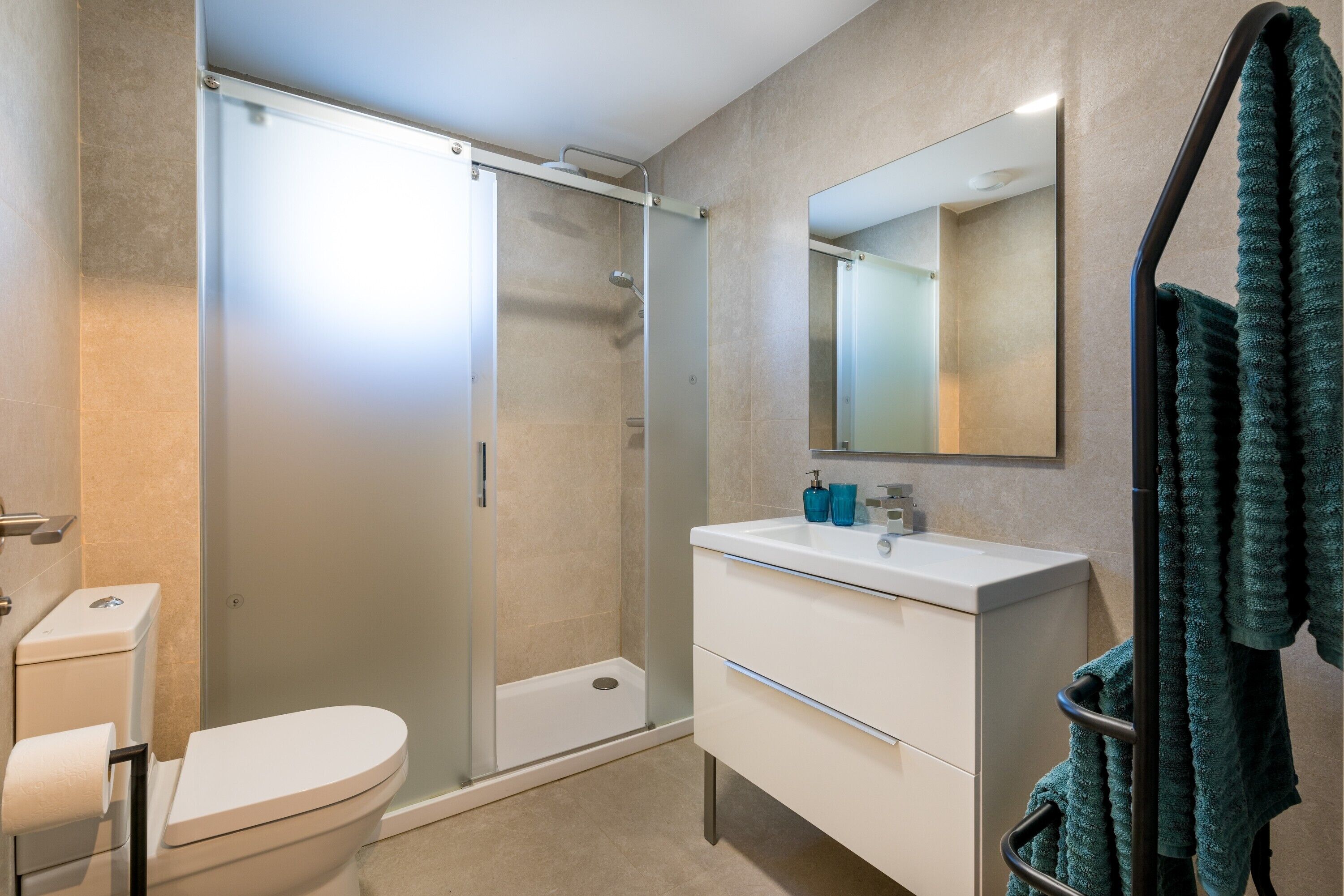 A modern bathroom with a glass shower enclosure, a toilet, a white sink with a mirror, and a towel rack.