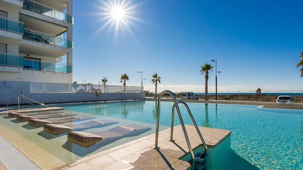 A swimming pool with clear blue water, a sun shining in the sky, and palm trees around. - Apartment DunaBeach close to the Sea, with Pool & Balcony (Torrox Costa)
