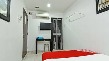 A small, clean room with a bed, a desk, a chair, a TV, and an air conditioning unit.