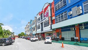 Vista de una calle con una hilera de edificios, incluyendo un hotel y un gimnasio. Hay coches aparcados y una motocicleta en la calle.