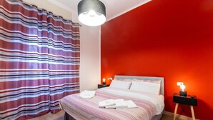 A hotel room with a bed, striped curtains, a red wall, and bedside lamps.