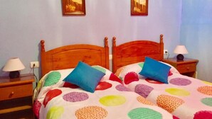A bedroom with a wooden bed, colorful polka dot bedding, two bedside lamps, and two framed pictures on the wall.