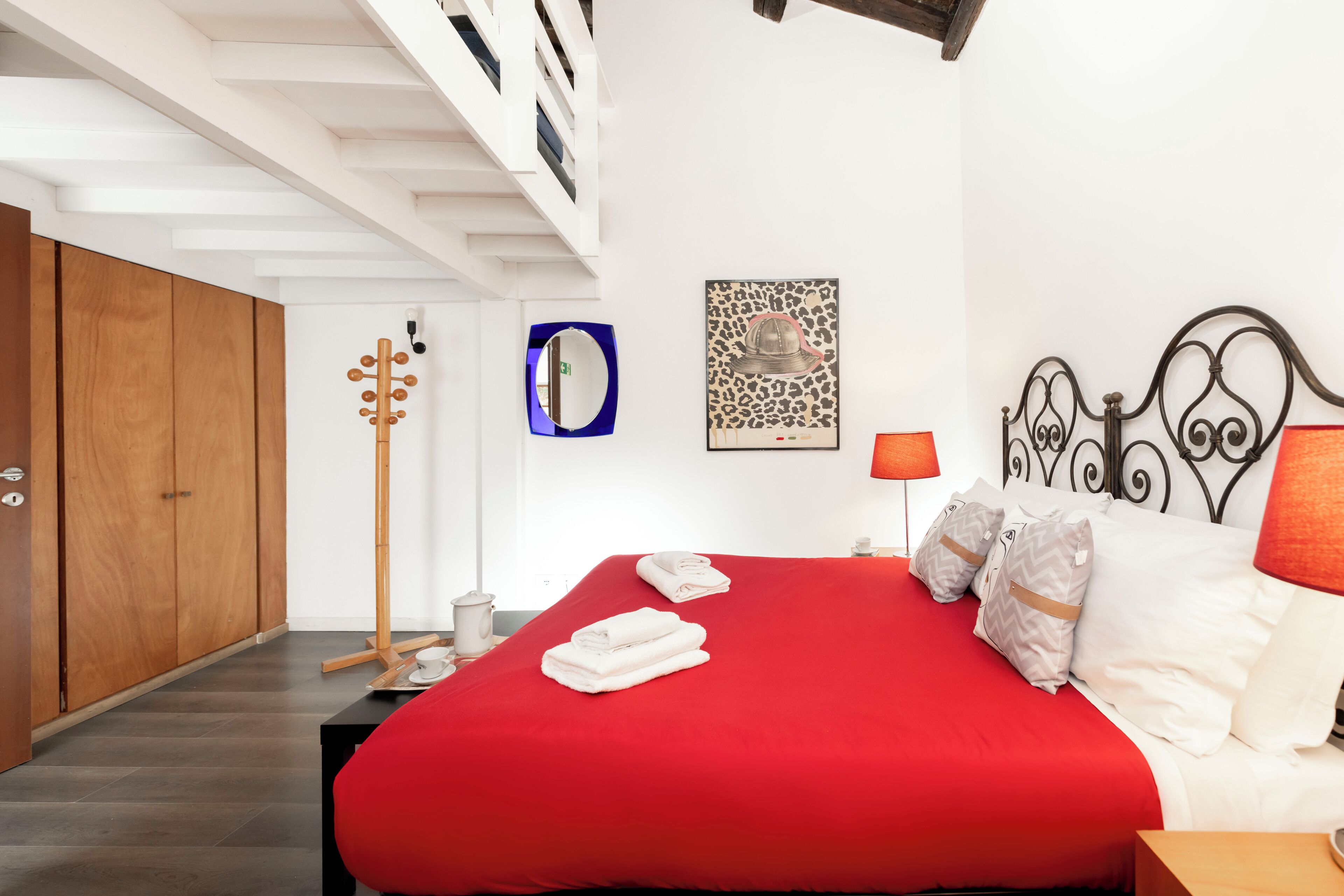A bedroom with a red bedspread, wooden wardrobe, and a mirror on the wall.