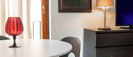 A hotel room with a round table, a single chair, a television, a lamp, and a painting on the wall.