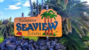 Placa para Kalapana SeaView Estates, palmeiras e céu claro ao fundo.