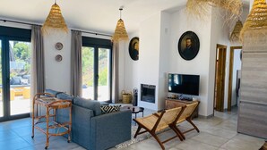 A modern living room with a grey sofa, wicker chairs, and a flat-screen TV. - Finca Loma La Tapia (Cómpeta)