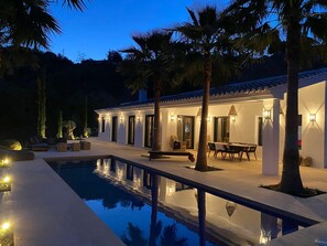 Una villa moderna con piscina, area salotto esterna e finestre illuminate.