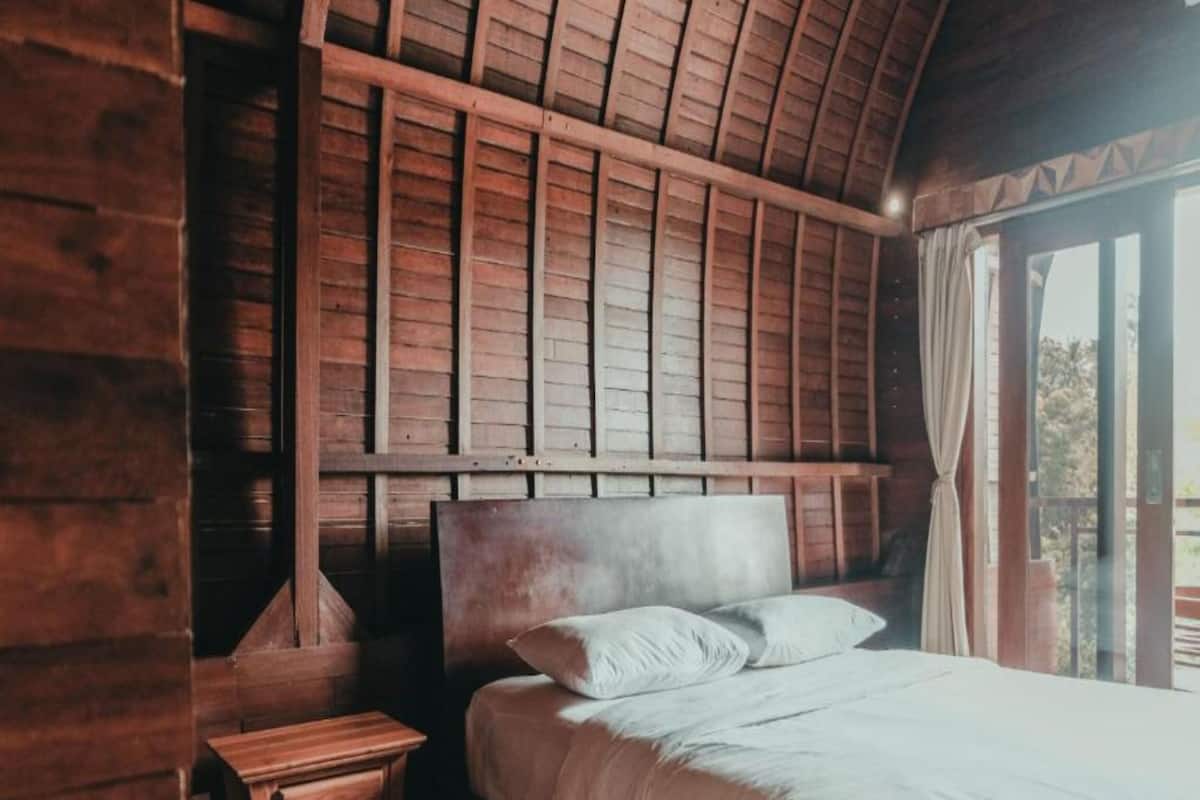 Una habitación de madera con cama, mesita de noche y ventana con cortinas.